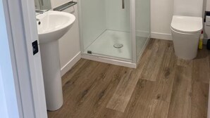 Et moderne badeværelse med en glasafskærmet brusekabine, et hvidt håndvaskarrangement og et toilet.