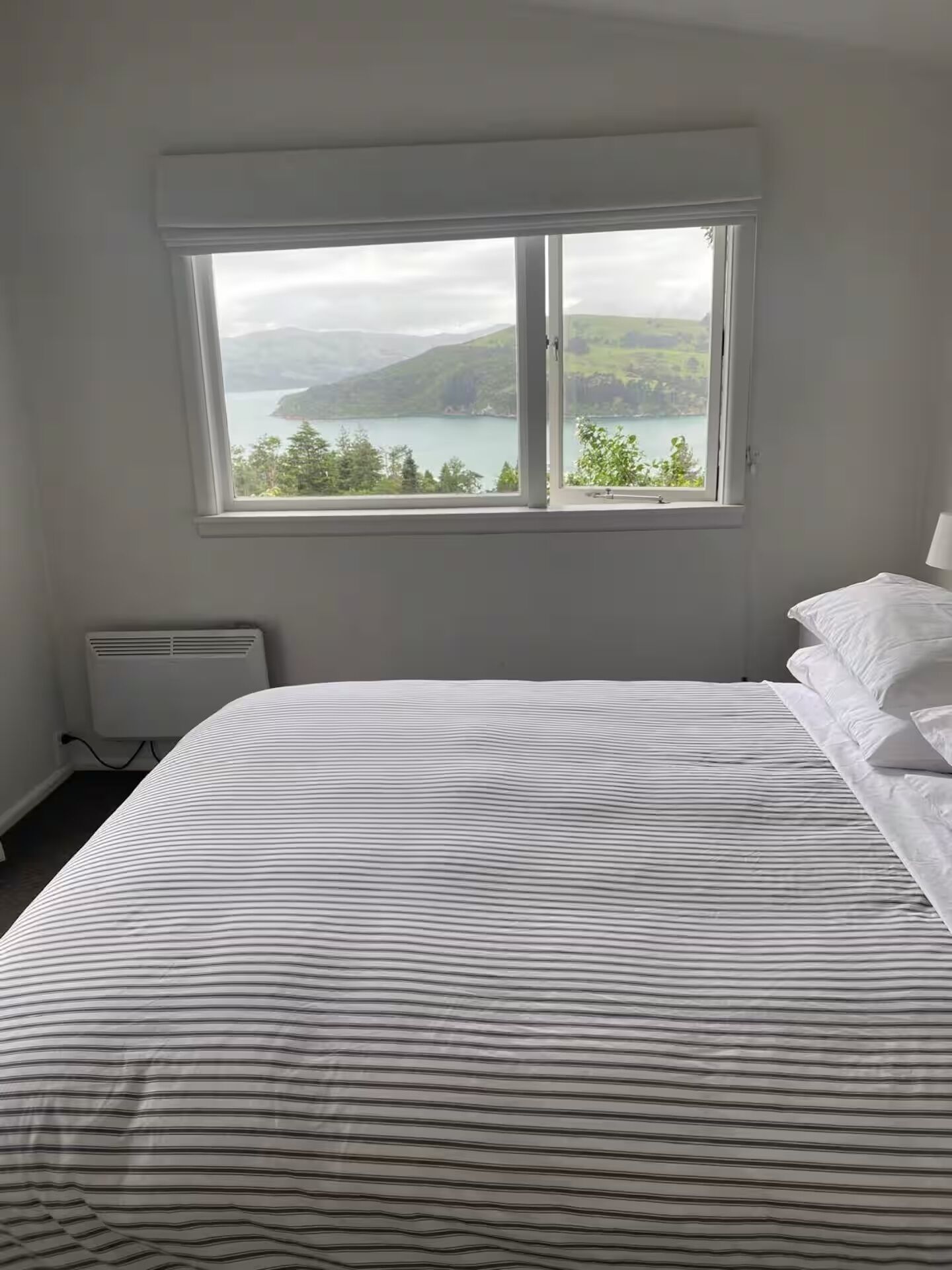Een slaapkamer met een groot bed, een raam met uitzicht op een meer en bergen, en een radiator.