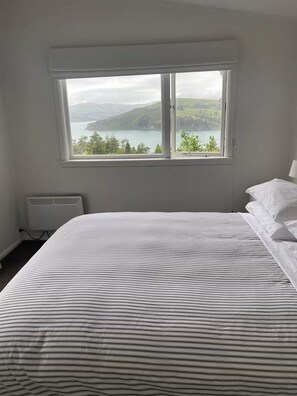 Ett sovrum med en stor säng, ett fönster med utsikt över en sjö och berg, och ett element.