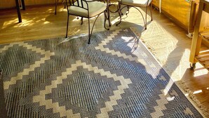A covered outdoor dining area with a table and chairs, a patterned rug, and a view of a lake.