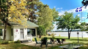 A small lodge with a porch, outdoor seating, and a view of a lake.