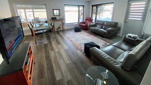 A modern living room with a glass TV stand, a leather sofa, a red armchair, and a dining area with a glass table and chairs.