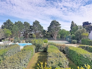 A landscaped garden with a pool, trees, and a tennis court.