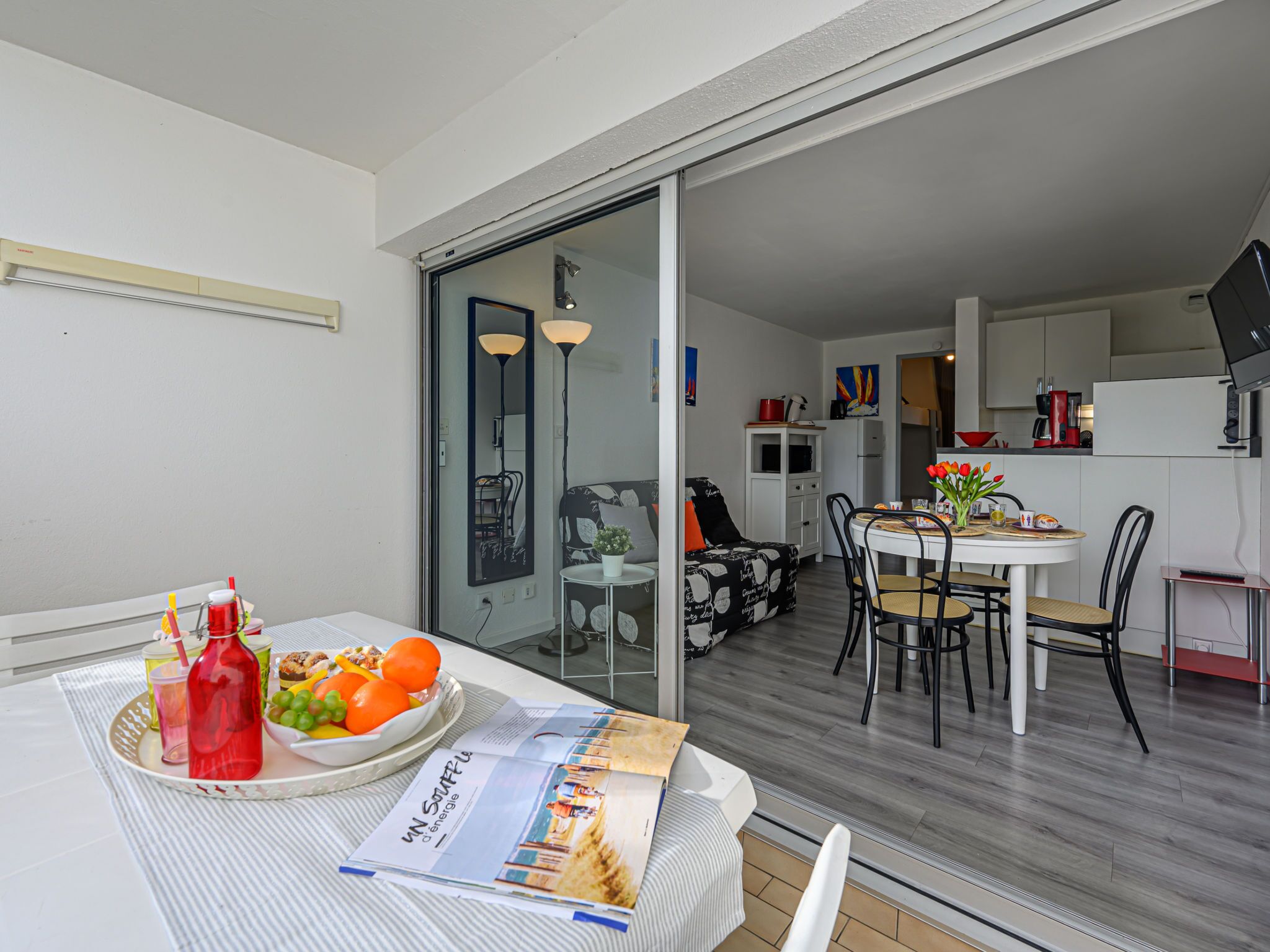 A modern apartment with a dining area, kitchenette, and a sliding glass door leading to a balcony.