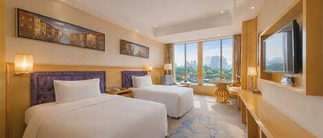 A hotel room with two beds, a desk, a TV, and large windows with a city view.
