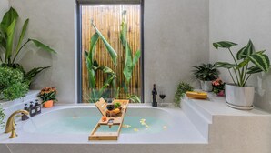 Ein modernes Badezimmer mit einer Badewanne, einer Holztablett mit Früchten und einer Flasche sowie verschiedenen Topfpflanzen.