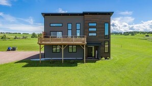 Une maison moderne à deux étages, dotée d’une terrasse en bois et de grandes fenêtres.