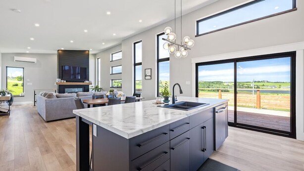 Une cuisine moderne dotée d’un grand îlot central, d’appareils électroménagers intégrés et offrant une vue sur l’extérieur.