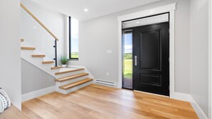 Un intérieur moderne avec un escalier en bois, une porte noire et une vue sur l’extérieur.