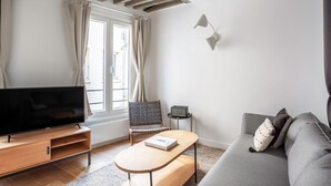 En moderne stue med et fladskærms-TV, en grå sofa, en vævet stol og et lille bord med en bog.