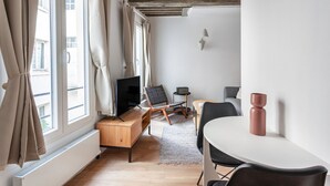 En moderne stue med et fjernsyn, træmøbler, et spisebord og et stort vindue med gardiner.