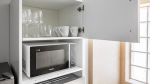 Une cuisine équipée d’un four à micro-ondes encastré et d’une étagère où sont rangés des verres et des tasses blanches.
