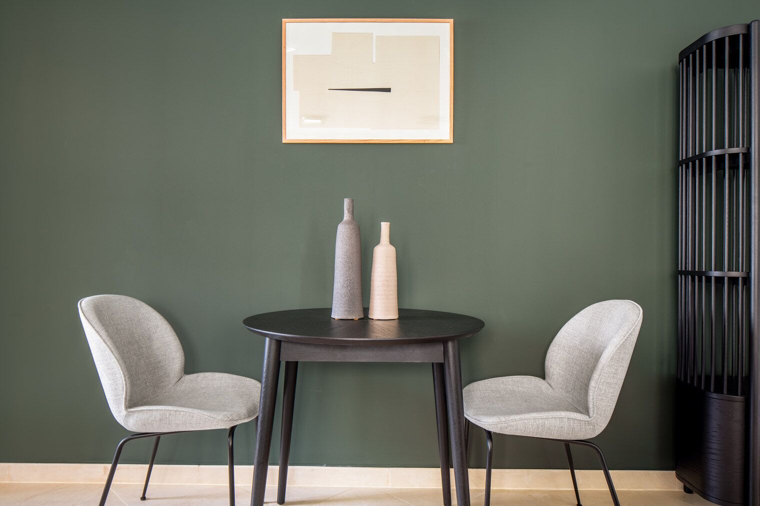 Une pièce avec deux chaises grises, une petite table ronde et deux vases posés sur la table.