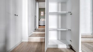 Un pasillo con paredes blancas y suelo de madera que conduce a un dormitorio con cama y mesita de noche.