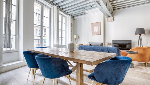 Una habitación amplia con una mesa de comedor de madera, sillas de terciopelo azul, un sofá y un televisor.