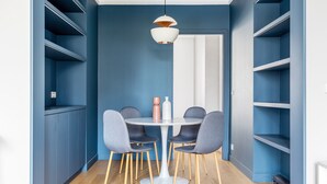 A dining area with a round table and four chairs, blue walls, and a hanging pendant light. - Blueground | Invalides, view of Matignon Gardens (Paris)