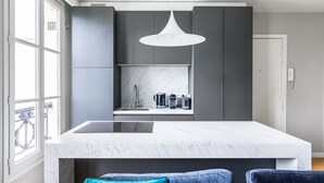 A modern kitchen with a large island, grey cabinetry, and a white pendant light. - Blueground | Invalides, view of Matignon Gardens (Paris)