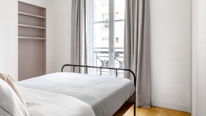 A bedroom with a bed, a wardrobe, and a window with curtains. - Blueground | Invalides, view of Matignon Gardens (Paris)
