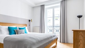 A neatly made bed with a grey blanket, a wooden headboard, and blue and grey pillows. - Blueground | Invalides, view of Matignon Gardens (Paris)