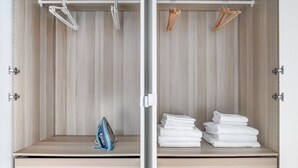 A wardrobe with wooden panels, a blue iron, and neatly folded white towels. - Blueground | Marais, next to Rivoli St shopping (Paris)