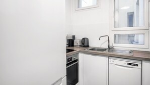 A compact kitchen with white cabinets, a stainless steel sink, a coffee maker, a toaster, and a dishwasher. - Blueground | Marais, next to Rivoli St shopping (Paris)