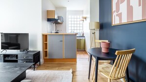 Une cuisine moderne dotée d’appareils électroménagers intégrés, un coin repas avec une table et des chaises, et une grande fenêtre laissant entrer la lumière naturelle.