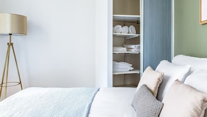 Une chambre à coucher avec un lit, des oreillers, une lampe de chevet et une armoire contenant des serviettes pliées.