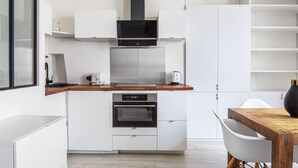 Une cuisine moderne avec des meubles blancs, une hotte noire, un four encastré et un plan de travail en bois.