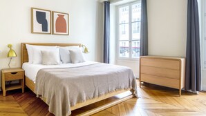 Une chambre bien rangée, avec un lit en bois, des tables de chevet, une commode et une fenêtre avec des rideaux.