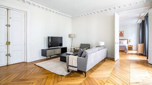 Un salon moderne doté d’un téléviseur à écran plat, d’un canapé gris et d’un parquet en bois.