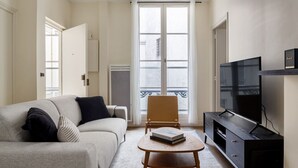 A living room with a sofa, a small table, a chair, a TV, and a fireplace. - Blueground | Madeleine, elev, near art (Paris)
