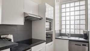 A modern kitchen with white cabinets, a black countertop, a built-in oven, a microwave, a coffee maker, and a window with frosted glass. - Blueground | Madeleine, elev, near art (Paris)