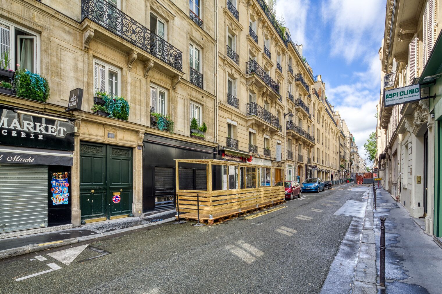 Una calle con un edificio que tiene una persiana cerrada a la izquierda y una estructura de madera a la derecha.