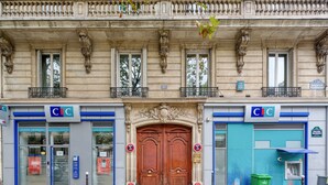 A building facade with two storefronts labeled 'CIC', a wooden double door entrance, and a green trash bin on the sidewalk.
