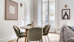 A modern living room with a dining area, featuring a round table, two chairs, a sofa, and artwork on the walls.