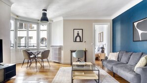 A modern living room with a grey sofa, a glass coffee table, and a dining area with chairs and a table. - Blueground | Arc de Triomphe, furnished, elevator (Paris)