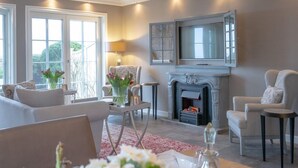 A modern living room with a fireplace, comfortable seating, a dining table set for four, and a large window providing natural light.