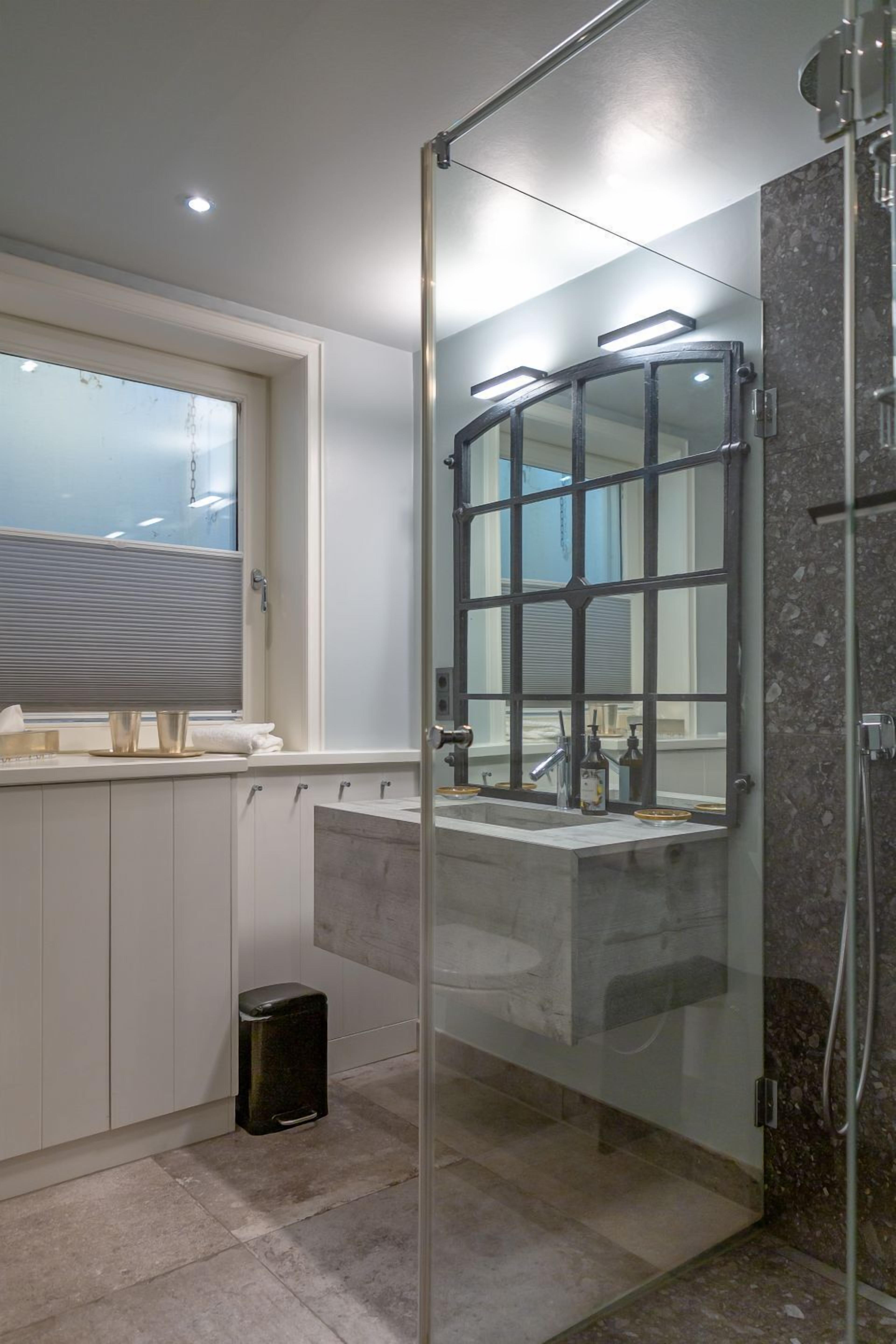 A modern bathroom with a glass-enclosed shower, a large mirror, and a window above the sink.