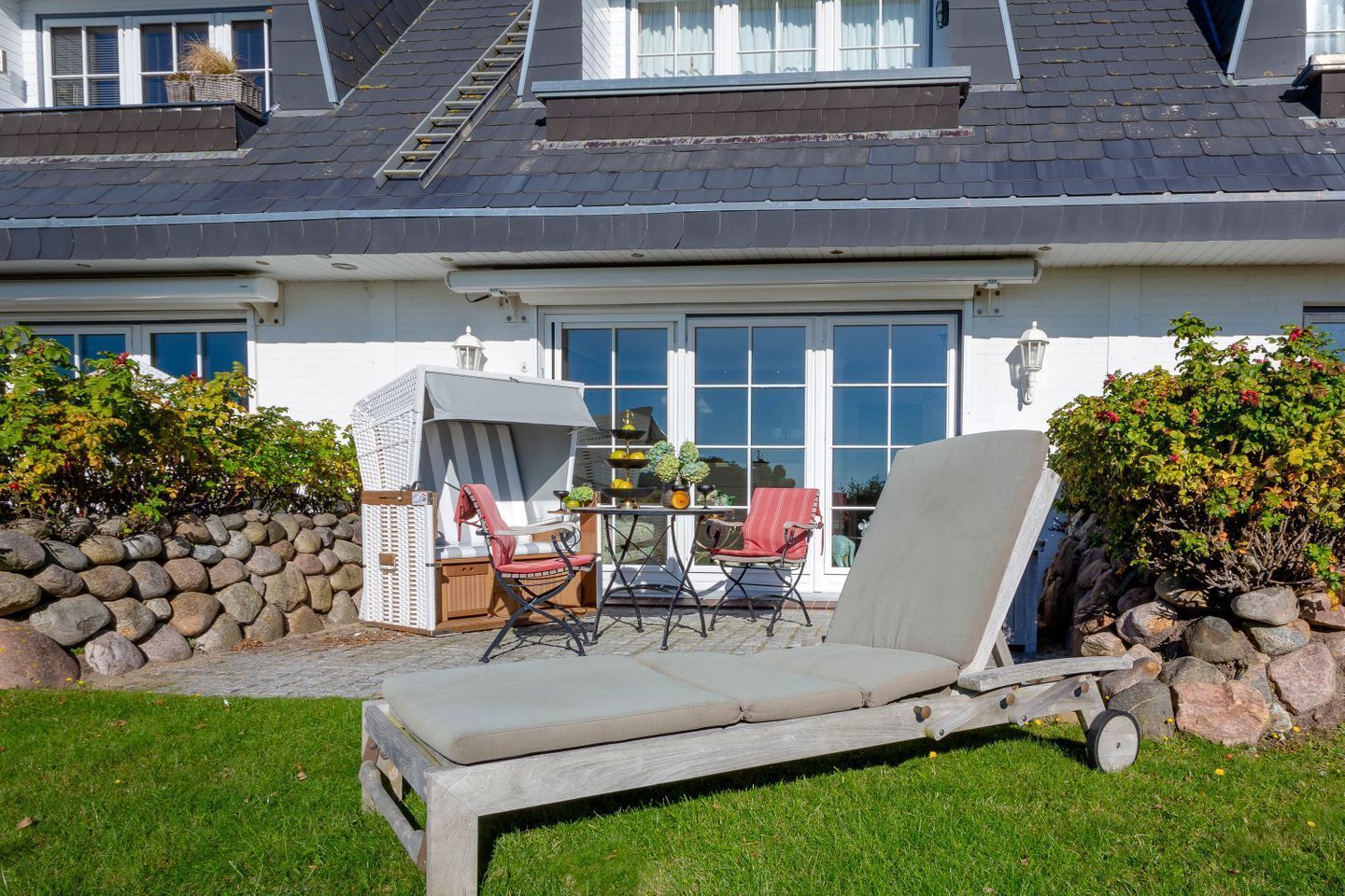 Una casa con un patio que incluye una silla de lounge, dos sillas de comedor y una mesita con una lámpara.