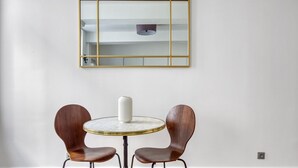 A room with a round table, two wooden chairs, a white vase, and a gold-framed mirror on the wall. - Blueground | Latin Quarter, nr Sorbonne (Paris)