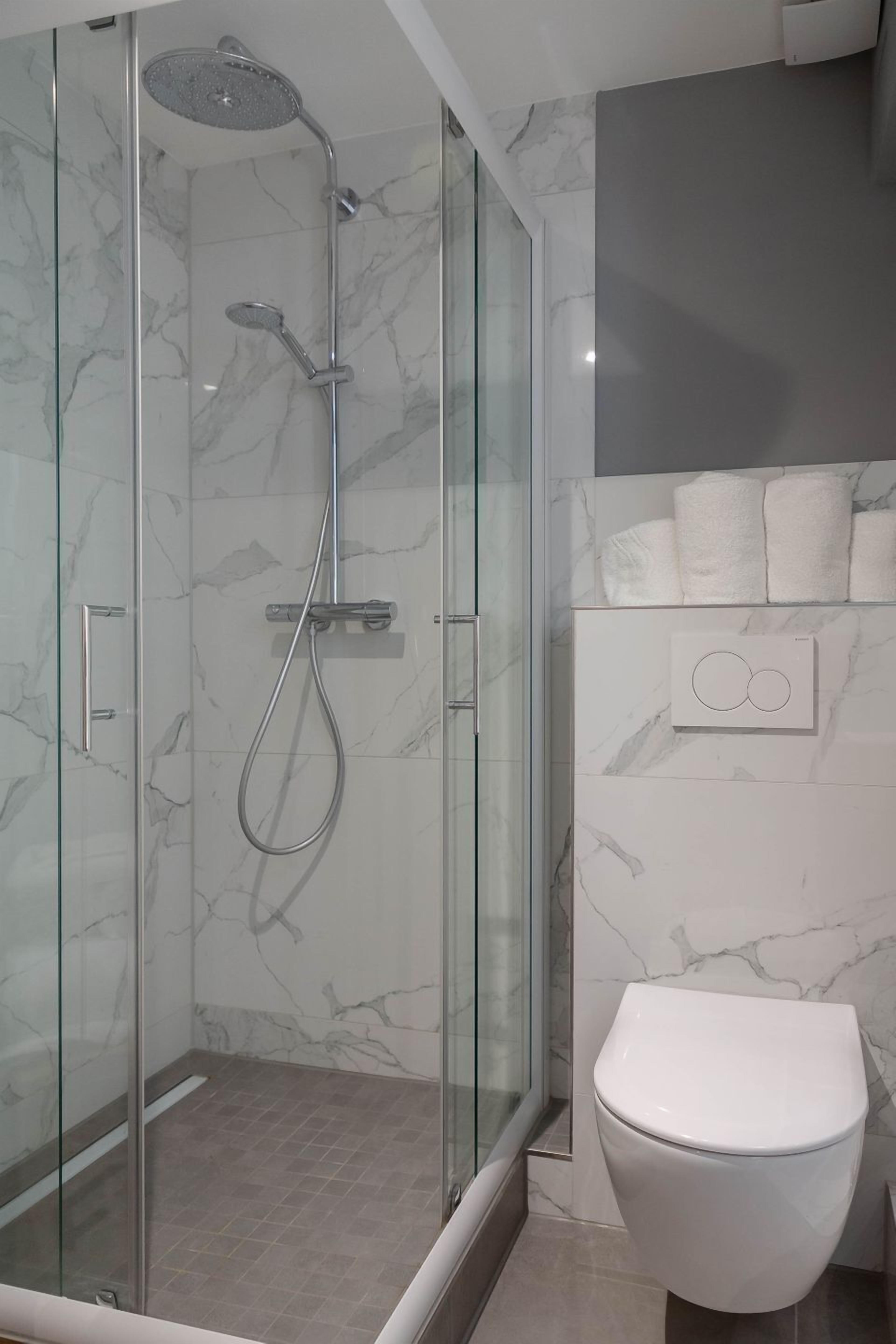 Un baño moderno con ducha envuelta en vidrio, inodoro blanco y paredes con diseño de mármol.