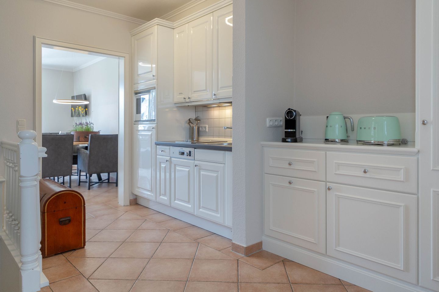 A kitchen with white cabinets, a tiled floor, and a coffee maker on the counter.