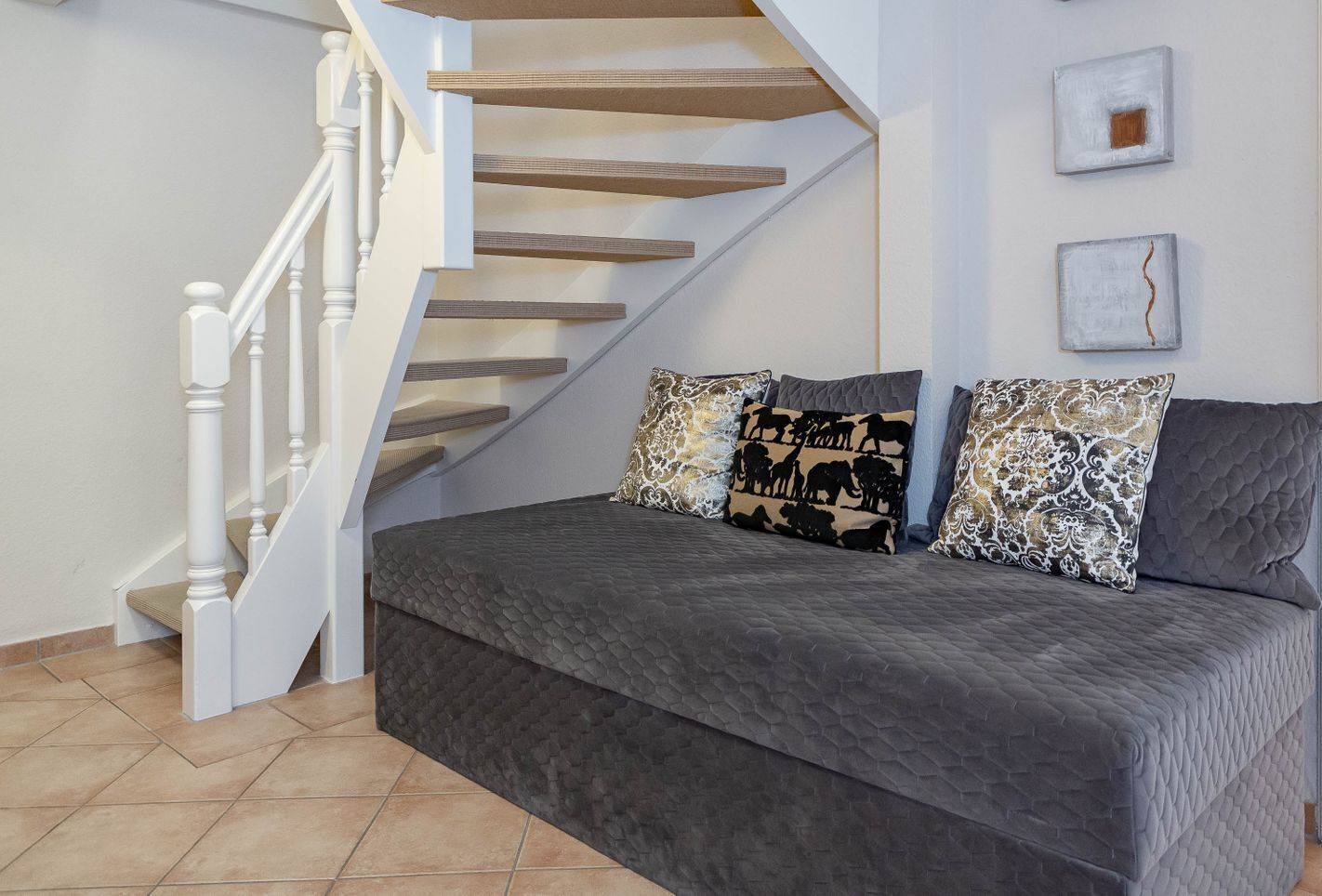 A modern living room with a grey sofa set, a white staircase, and two wall art pieces.