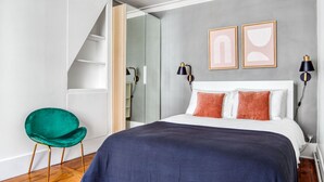 Ein modernes Schlafzimmer mit einem großen Bett, einem grünen Sessel und einem begehbaren Kleiderschrank.