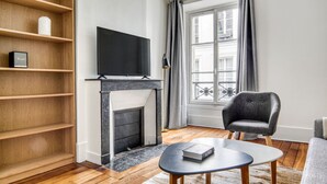 Ein Wohnzimmer mit Kamin, Fernseher, Bücherregal, Sessel und Tisch.