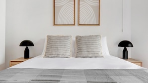Un dormitorio moderno con una cama grande, dos mesitas de noche, dos lámparas y dos cuadros colgados en la pared.