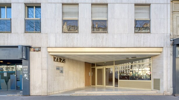 Un edificio con fachada moderna, amplia entrada de vidrio y un cartel con la dirección.