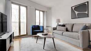 Una sala de estar moderna con un sofá gris, un sillón azul, una mesa de centro y un televisor sobre un mueble de madera.