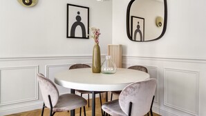 Une table de salle à manger ronde, accompagnée de quatre chaises, un vase rempli de fleurs et deux œuvres d’art encadrées accrochées au mur.