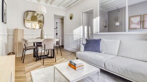 Un salon moderne avec un canapé blanc, une table à manger avec des chaises, une table basse et un grand miroir au mur.